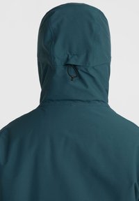Veste imperméable teal avec capuche, dotée d'un réglage par cordon. Texture lisse et design minimaliste, sans logos ni motifs visibles.