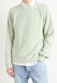 Maglione a costine verde chiaro con colletto rotondo e maniche raglan. Presenta un logo sottile sul petto e un motivo testurizzato.