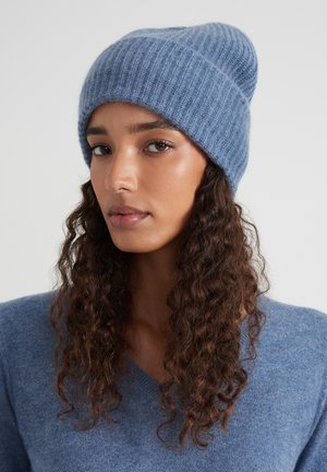 Blauwe geribbelde gebreide beanie met een zachte textuur, met een slouchy ontwerp dat naar boven toe smal wordt. Draagt bij een bijpassende blauwe trui.