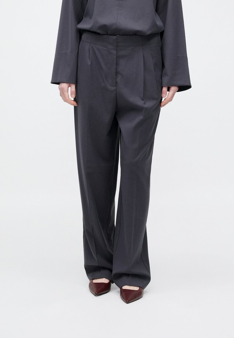 Σκούρο γκρι παντελόνι με πιέτες, κατασκευασμένο από απαλό ύφασμα. Φοριέται με μυτερά μπορντό παπούτσια, που έχουν κομψό σχεδιασμό.