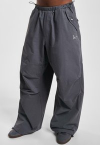 Šedé oversized kalhoty vyrobené z lehkého materiálu, s elastickým pasem, bočními kapsami a decentním potiskem na přední straně.