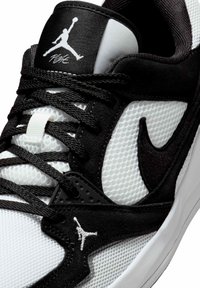 Gros plan d'une chaussure Air Jordan noir et blanc montrant des lacets noirs, une tige en mesh, le logo Nike swoosh, et le logo Jumpman sur la languette et le côté.