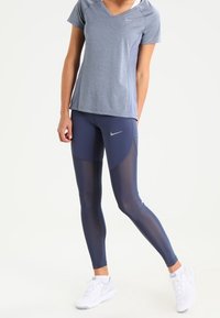 Marinblå sportleggings med meshpaneler, kombinerade med en ljusblå t-shirt med v-ringning. Båda tillverkade av andningsbart material och har diskreta varumärkeslogotyper.