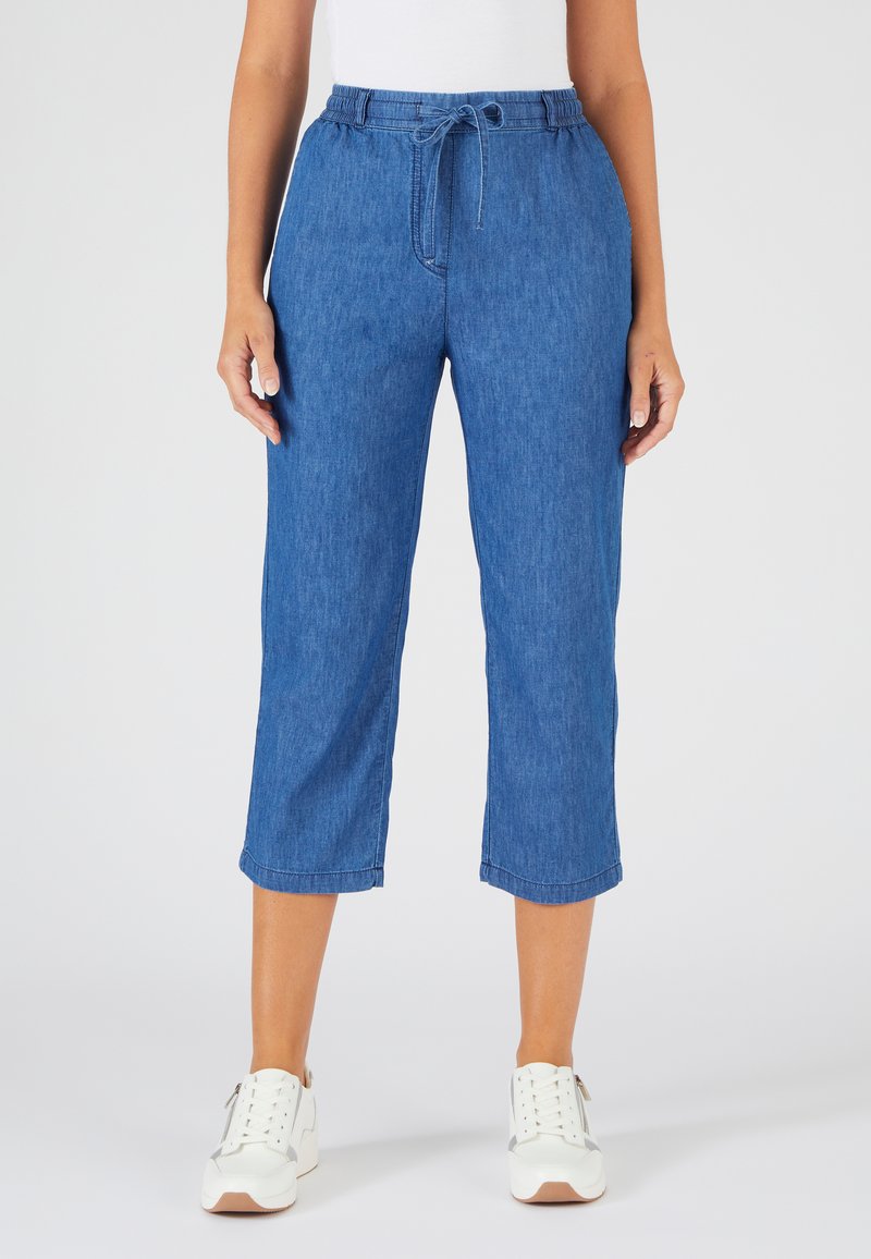 Pantalones cortos de color azul claro, tipo mezclilla, con cintura elástica, cordón y puños. Combinados con zapatillas blancas.