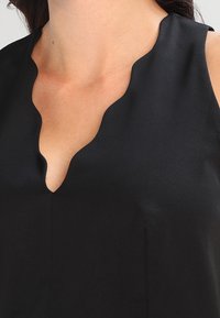 Black sleeveless top with a scalloped neckline, made of smooth fabric, showcasing a simple design and clean lines. Minimalistic aesthetic.