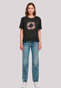 Black cotton t-shirt with a floral design in pink and white, short sleeves, relaxed fit, paired with light wash denim jeans and white sneakers.