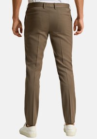 Pantaloni marroni su misura con una texture liscia, vestibilità slim e due tasche posteriori. Abbinati a sneaker bianche, che mostrano uno stile casual.