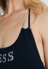 Vêtement noir sans manches, orné d'accents en strass transparents sur les bretelles et d'un détail froncé au niveau du col.
