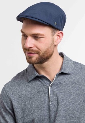 Căciulă de marină din țesătură, cu o formă plată și un buton mic pe lateral. Purtați cu un tricou polo gri, având o textură heather.