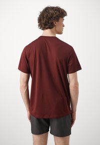 Bordå kortermet t-skjorte med rund hals, glatt tekstur og avrundet nederkant. Båret med mørke shorts, vist fra baksiden.