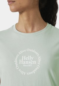 Camiseta de algodón verde claro con un gráfico circular blanco que presenta el texto "Helly Hansen" y la frase "Vivo al aire libre desde 1877".