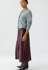 Lichtgrijze gebreide cardigan met ronde hals en knoopsluiting, gecombineerd met een bordeauxleren rok met een zijsplit en trekkoorddetail.