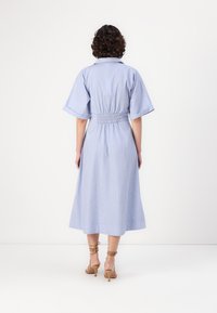 Abito midi a righe blu con maniche corte, vita elastica e gonna a campana; abbinato a sandali con tacco color nocciola.