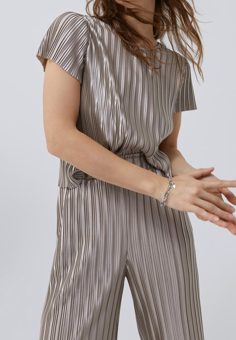 Blusa metálica plateada con rayas verticales, mangas cortas y un corte relajado, combinada con pantalones anchos a juego. Pulsera plateada como acento.