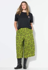 Zwarte t-shirt met roze hartdetail, gecombineerd met groene wijde broek met een bloemmotief. Draag het met zwarte cowboy-achtige laarzen.