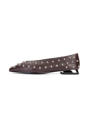 Zapato plano marrón oscuro con tachuelas redondas plateadas que cubren uniformemente la superficie y un pequeño tacón geométrico de bloque.