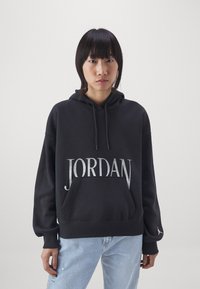 Sudadera negra con bolsillo frontal, que presenta un gran lettering en plata "JORDAN". Tejido de mezcla de algodón, corte relajado y puños acanalados.