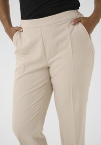 Beige tailored trousers featuring a smooth texture, side pockets, and a straight-leg design. Made from lightweight, breathable fabric.