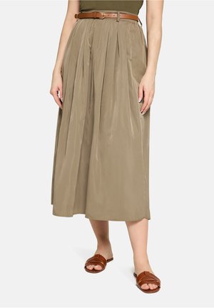 Jupe plissée longueur genoux en kaki clair avec une ceinture élastique, ceinture en cuir marron, et associée à des sandales slides marron.