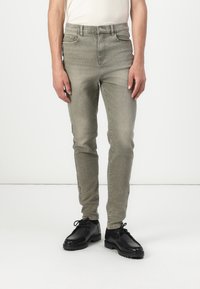 Jeans slim-fit de un verde olive deschis cu o ușoară elasticitate, design cu cinci buzunare și închidere clasică cu nasture. Purtați cu pantofi negri cu șiret.