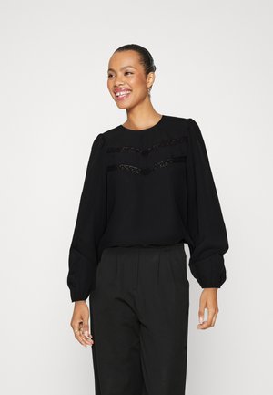 Black blouse with puffed sleeves, featuring textured black stripes across the front. Paired with high-waisted black trousers.