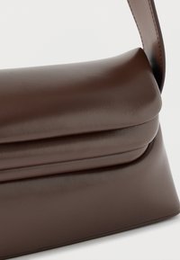 Καφέ λείο δερμάτινο τσάντα χειρός με κλείσιμο με καπάκι και φαρδύ ιμάντα ώμου σε λευκό φόντο.