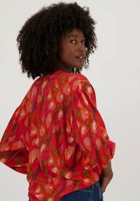 Rood en oranje gebloemd blouse met losse, opbollende mouwen en een ronde halslijn, gemaakt van lichtgewicht, vloeiende stof.