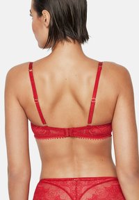 Rode kanten beha met verstelbare bandjes, voorzien van decoratieve rand, een haak-en-oogsluiting en een getextureerd patroon op de stof.