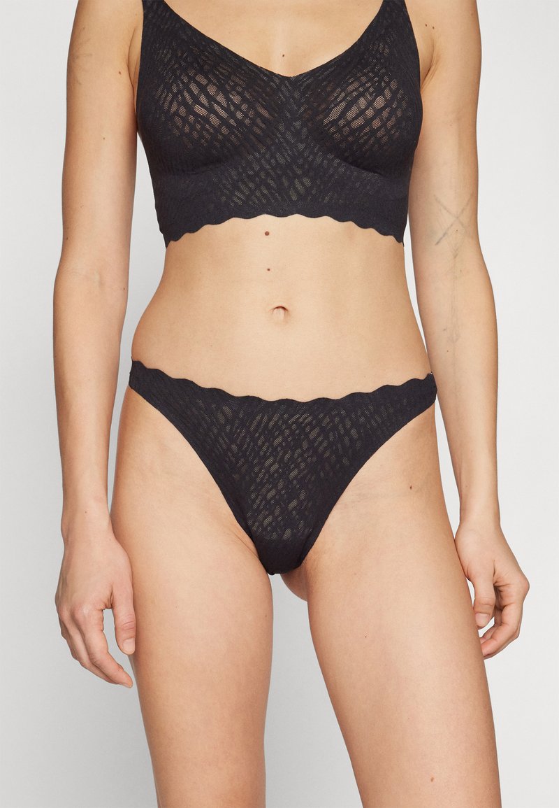 Black bra and thong set made of textured lace with a geometric pattern, featuring scalloped edges and a smooth finish.