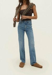 Jeans azul de cintura alta con un lavado claro, diseño de pierna recta, estilo clásico de cinco bolsillos, combinados con un chal de punto marrón sobre una blusa ajustada.