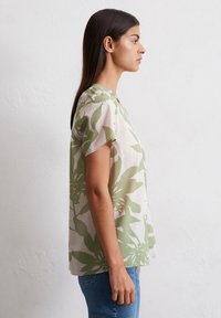 Blouse à manches courtes en beige clair avec motif floral vert, tissu léger, coupe décontractée et col rond.