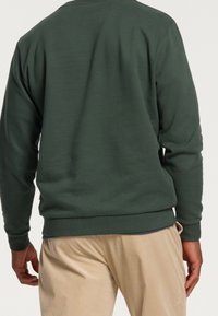 Mörkgrön sweatshirt med rund halsringning, ribbade muddar och nederkant, kombinerad med ljusbeige kordbyxor. Mjuk tyg och avslappnad passform.