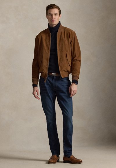 Braune Wildleder-Bomberjacke, marineblauer Rollkragenpullover, dunkle Jeans und braune Lederschuhe. Einfaches Design mit geknöpften Taschen und gerippten Bündchen.