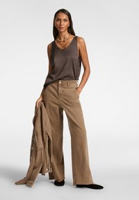 Top in satin marrone e pantaloni a gamba larga beige. L'outfit è abbinato a una giacca coordinata, con decorazioni, e ballerine nere.