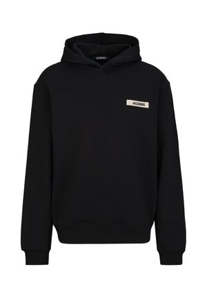 Sweat à capuche noir à manches longues avec une petite étiquette rectangulaire indiquant "JACQUEMUS" sur la poitrine gauche.