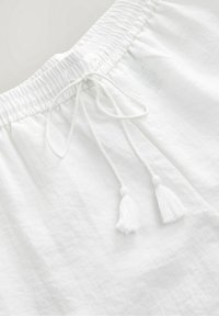 Gros plan sur un short en tissu blanc avec une taille élastique et un cordon tressé décoratif se terminant par des pompons.