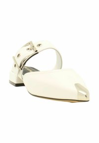 Chaussure plate blanche avec un bout pointu, présentant un accent métallique à la pointe et une sangle à boucle à la cheville. Texture lisse, talon bas.