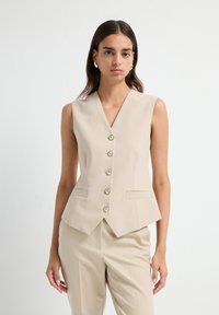Blazer sans manches beige avec un décolleté en V plongeant, fermeture à cinq boutons à l'avant et deux poches latérales ; tissu lisse avec une coupe ajustée.