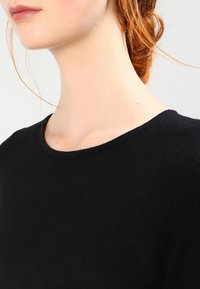 Svart tröja med rund hals och korta ärmar, med en mjuk textur och ett fint stickat mönster.