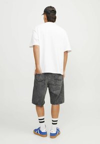 Mies, który nosi czapkę w kolorze czarnym, białą koszulkę, czarne dżinsowe szorty, białe skarpetki w czarne paski i niebieskie sneakersy, stoi plecami.