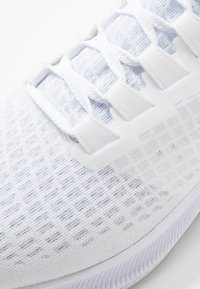 Scarpa da ginnastica bianca con tomaia in mesh, caratterizzata da sottili accenti blu chiaro, un motivo testurizzato, lacci piatti e una suola ammortizzata.