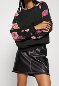Černá mikina s květinovým potiskem v růžové a fialové barvě na rukávech, doplněná o upnutou černou koženou mini sukni s bílými šitími detaily.
