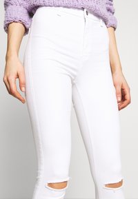 Jeans skinny blancos con cortes desgastados en las rodillas. Fabricados con tela de denim, presentan una cintura alta y una textura suave.