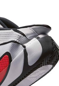 Primer plano del talón de un zapato deportivo en colores blanco, negro y rojo con suela texturizada y logo Jumpman en la suela de goma negra.