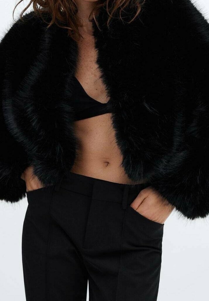 Sort faux fur cropped jakke med et voluminøst design, parret med en sort top og højttaljede bukser, der fremhæver en glat tekstur.
