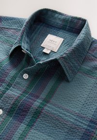 Grønternet skjorte med tekstureret stof, med en knappet krave, hvide knapper og en etiket med teksten "NEXT Tailoring, Regular Fit."
