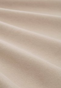 Tissu texturé beige avec un motif tissé subtil, affichant de douces vagues et une surface lisse, idéal pour diverses applications textiles.