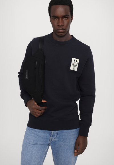 Merimieshuppari, jossa on paikka, jossa on pyöräikoni. Yhdistetty vaaleansinisiin farkkuihin ja mustaan olkalaukkuun. Sileä kankaan rakenne.