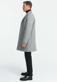 Hallhallane hall kasukas, millel on tekstuuriline muster, nurgelised kraed ja sirge lõige. Kombineeritud mustade kitsaste pükste ja mustade kingadega.