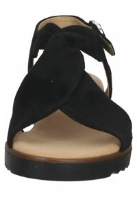 Sandale en suède noir avec un design noué à l'orteil, une bride de cheville réglable et une semelle en caoutchouc plate avec une légère accentuation boisée.